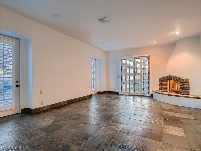 unfurnished living room with a healthy amount of sunlight, a brick fireplace, and dark tile floors