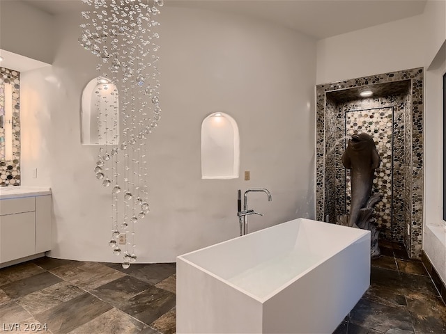 full bath featuring vanity, a freestanding tub, and stone tile flooring