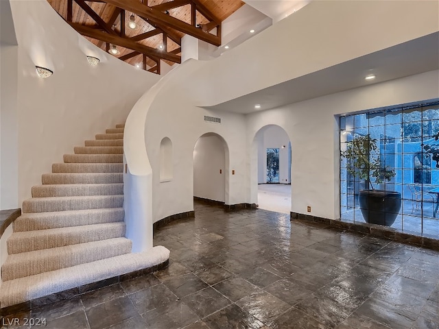 staircase with visible vents, high vaulted ceiling, stone finish flooring, arched walkways, and baseboards