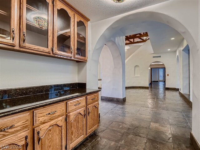 kitchen featuring a textured ceiling, dark stone countertops, and dark tile floors