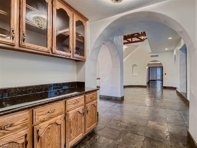 kitchen featuring glass insert cabinets, baseboards, stone tile flooring, arched walkways, and a textured ceiling