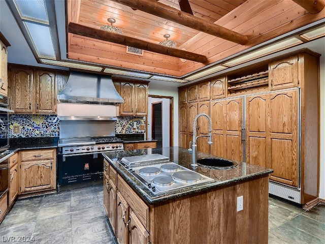 kitchen featuring dark tile floors, a center island with sink, tasteful backsplash, wall chimney exhaust hood, and wood ceiling