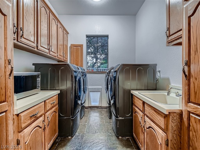 laundry room with a sink, washer and dryer, stone tile flooring, cabinet space, and a textured wall