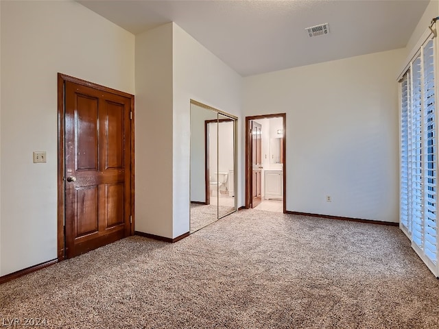 unfurnished bedroom featuring ensuite bath, carpet, visible vents, and baseboards