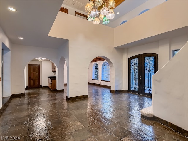 tiled foyer featuring a chandelier, french doors, a high ceiling, and a raised ceiling