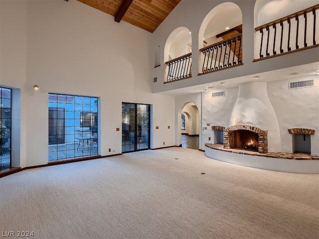 unfurnished living room featuring visible vents, baseboards, carpet, a lit fireplace, and wooden ceiling