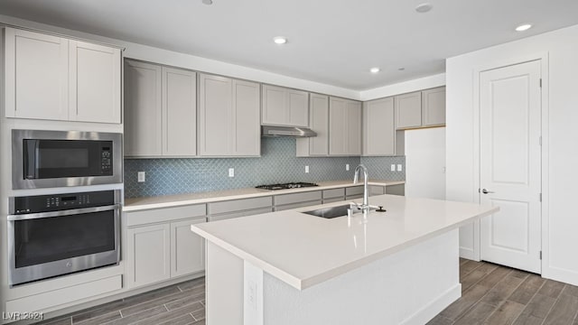 kitchen with appliances with stainless steel finishes, gray cabinets, sink, and a center island with sink