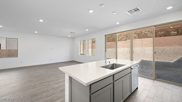 kitchen featuring an island with sink, sink, gray cabinetry, and stainless steel dishwasher