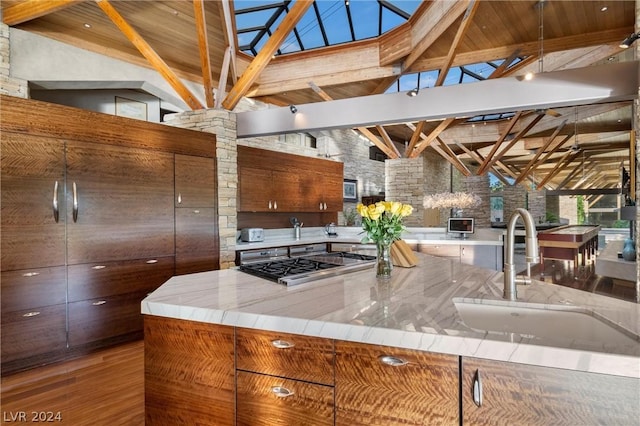 kitchen featuring high vaulted ceiling, sink, hardwood / wood-style flooring, stainless steel gas cooktop, and beam ceiling