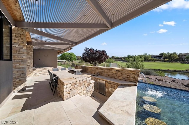 view of patio featuring a bar, a water view, a pergola, and exterior kitchen