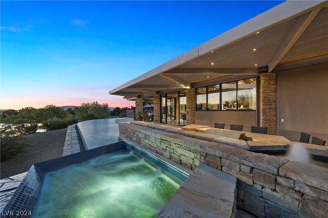 pool at dusk featuring an in ground hot tub