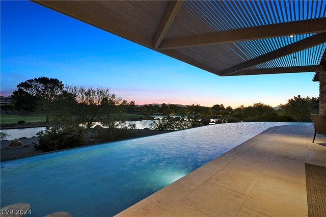 pool at dusk featuring a patio and a water view