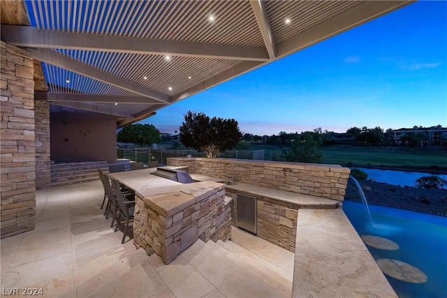 patio terrace at dusk with exterior bar, an outdoor kitchen, and a pergola