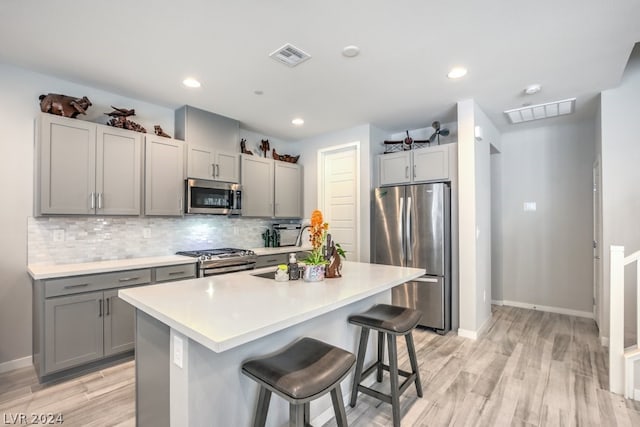 kitchen featuring sink, stainless steel appliances, an island with sink, gray cabinets, and a breakfast bar