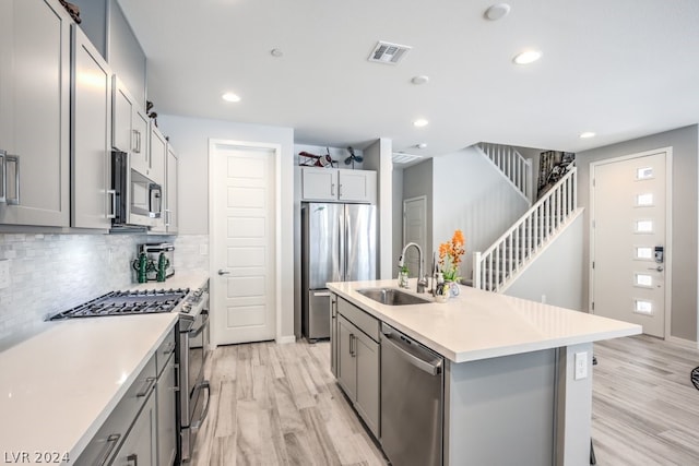 kitchen with gray cabinetry, sink, a kitchen island with sink, and appliances with stainless steel finishes