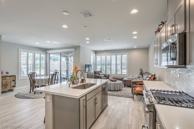 kitchen featuring sink, stainless steel appliances, light hardwood / wood-style flooring, gray cabinets, and a kitchen island with sink