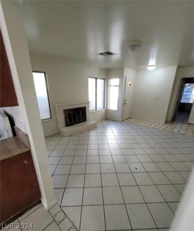 unfurnished living room with a brick fireplace and light tile patterned floors