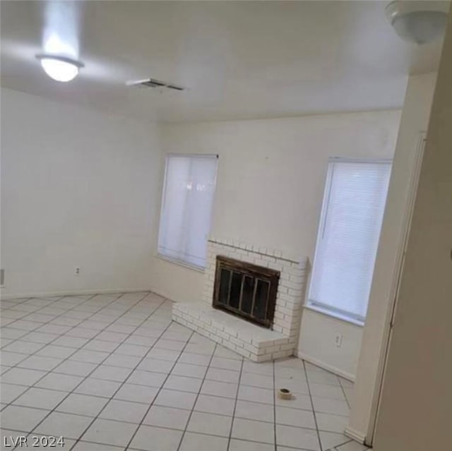 unfurnished living room with a brick fireplace and light tile patterned floors