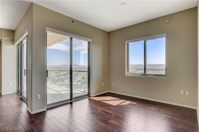 spare room featuring dark wood-type flooring, a mountain view, and baseboards