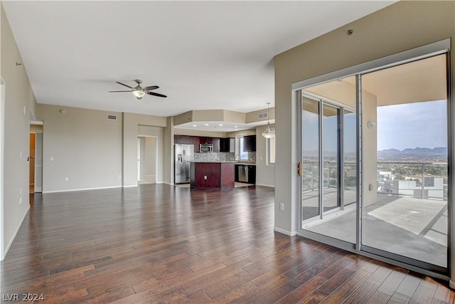 unfurnished living room featuring a mountain view, dark wood-style flooring, visible vents, baseboards, and a ceiling fan