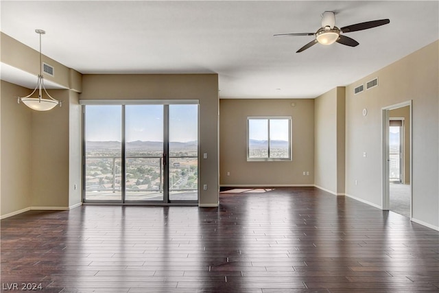 unfurnished room featuring dark wood-type flooring, a wealth of natural light, a mountain view, and baseboards