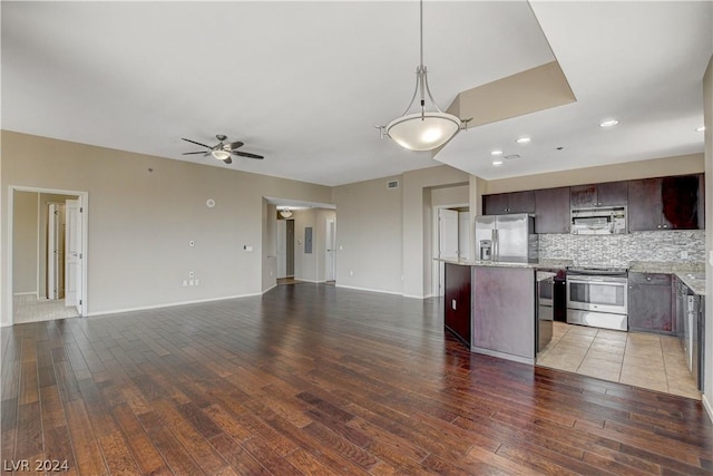 kitchen featuring dark brown cabinetry, stainless steel appliances, a kitchen island, open floor plan, and decorative backsplash