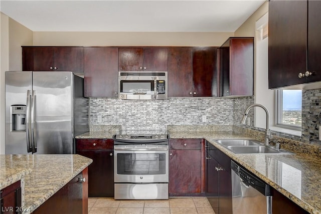 kitchen featuring light tile patterned floors, decorative backsplash, appliances with stainless steel finishes, a sink, and light stone countertops