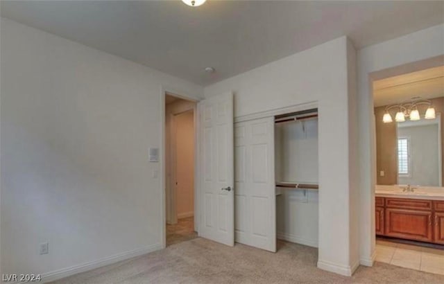 unfurnished bedroom featuring light carpet, ensuite bath, a closet, and sink