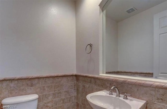 bathroom featuring toilet, sink, and tile walls