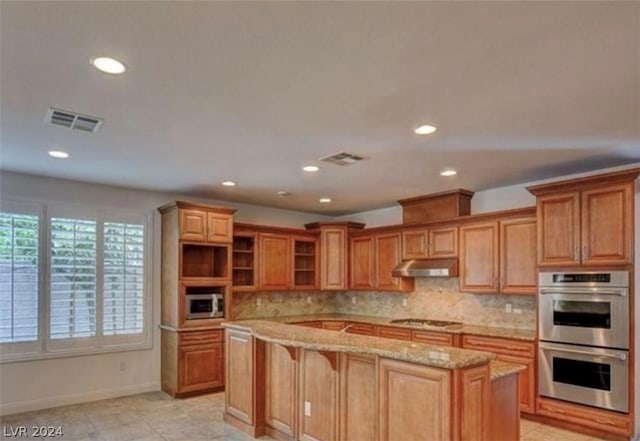 kitchen with a center island, decorative backsplash, light stone countertops, appliances with stainless steel finishes, and a breakfast bar area