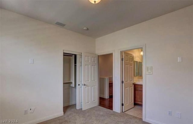 unfurnished bedroom with ensuite bath, a closet, and light colored carpet