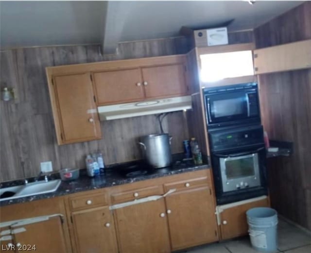 kitchen with black appliances, dark stone counters, wooden walls, light tile patterned floors, and beam ceiling