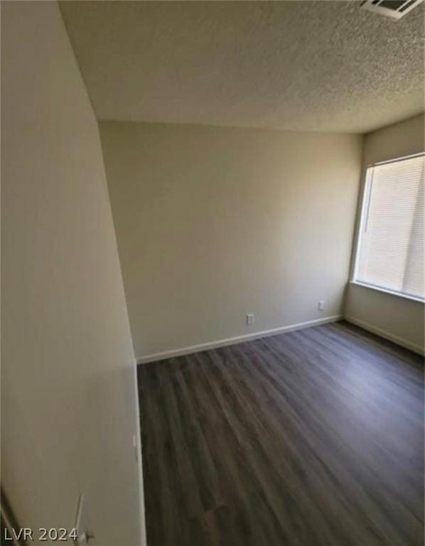 spare room featuring a textured ceiling and dark hardwood / wood-style flooring