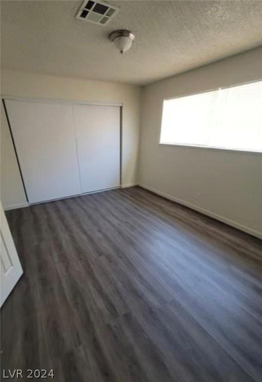 unfurnished bedroom with a closet, dark wood-type flooring, and a textured ceiling