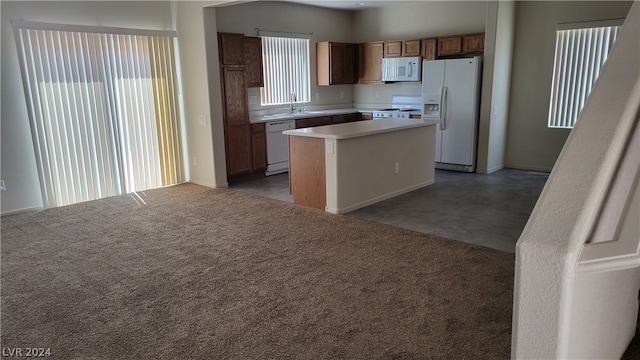 kitchen with white appliances, sink, dark tile flooring, and a kitchen island