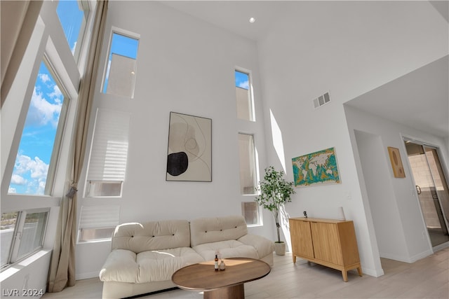 living room with a wealth of natural light, a towering ceiling, and light wood-type flooring