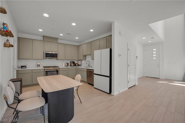 kitchen with light hardwood / wood-style flooring, a kitchen island, a kitchen breakfast bar, appliances with stainless steel finishes, and sink