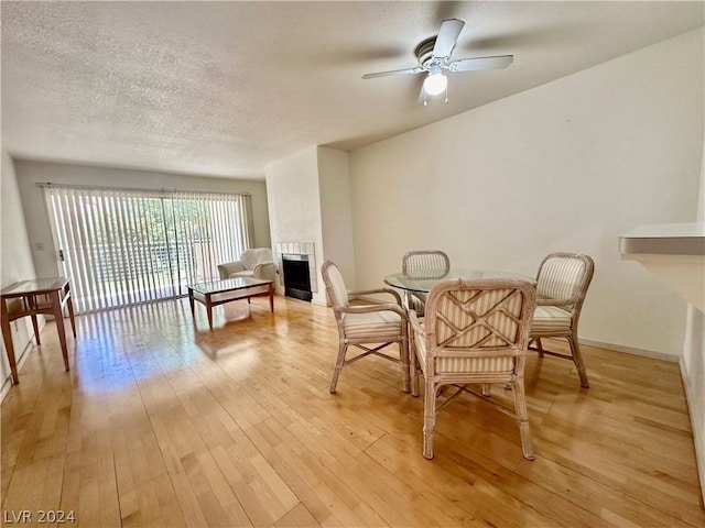 dining area featuring a textured ceiling, light hardwood / wood-style floors, ceiling fan, and a tiled fireplace