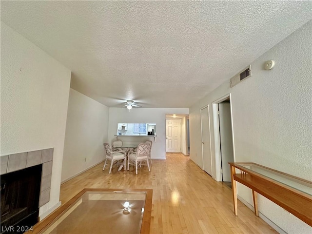 living room with ceiling fan, a textured ceiling, a tile fireplace, and light hardwood / wood-style flooring