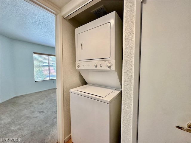 clothes washing area featuring a textured ceiling, stacked washer and dryer, and light colored carpet