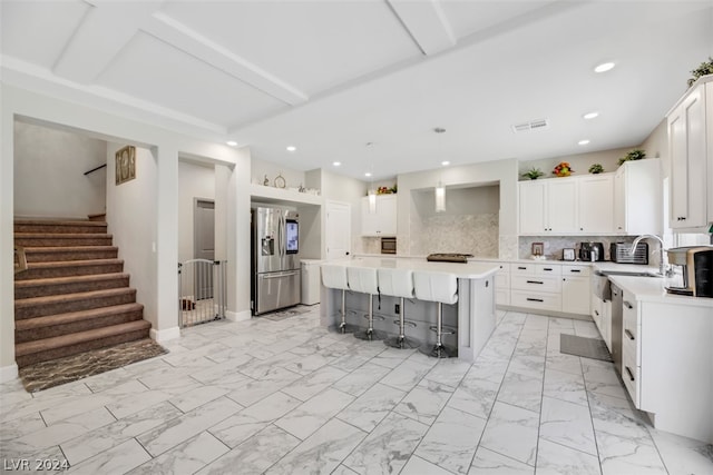 kitchen with a kitchen island, backsplash, a kitchen breakfast bar, white cabinetry, and stainless steel fridge