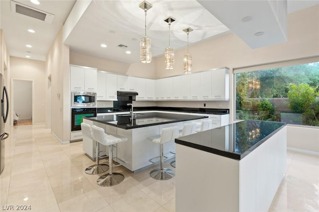 kitchen with appliances with stainless steel finishes, decorative light fixtures, white cabinetry, an island with sink, and a kitchen bar