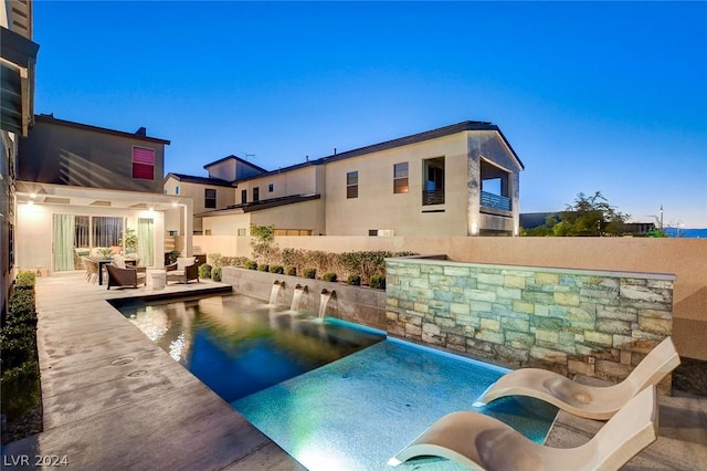 pool at dusk with pool water feature and a patio