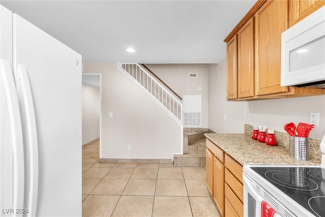 kitchen featuring light tile patterned flooring, light stone countertops, and white appliances