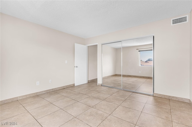 unfurnished bedroom with a closet, a textured ceiling, and light tile patterned floors