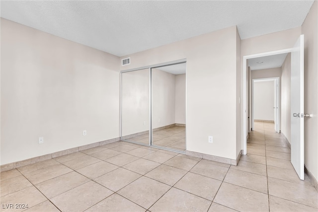 unfurnished bedroom with a textured ceiling, a closet, and light tile patterned floors