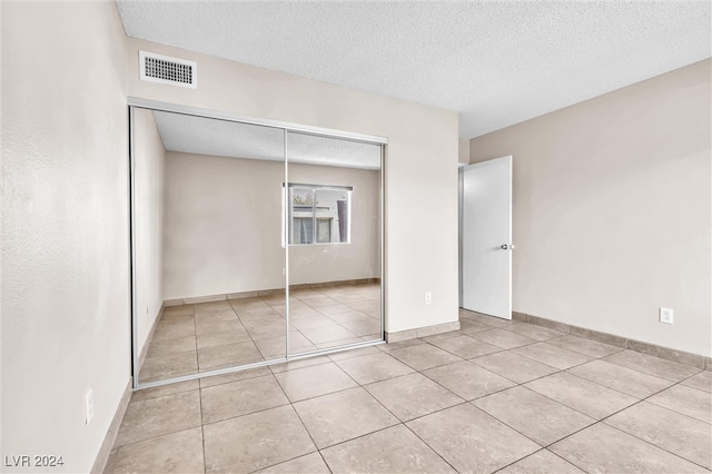 unfurnished bedroom with light tile patterned flooring, a closet, and a textured ceiling