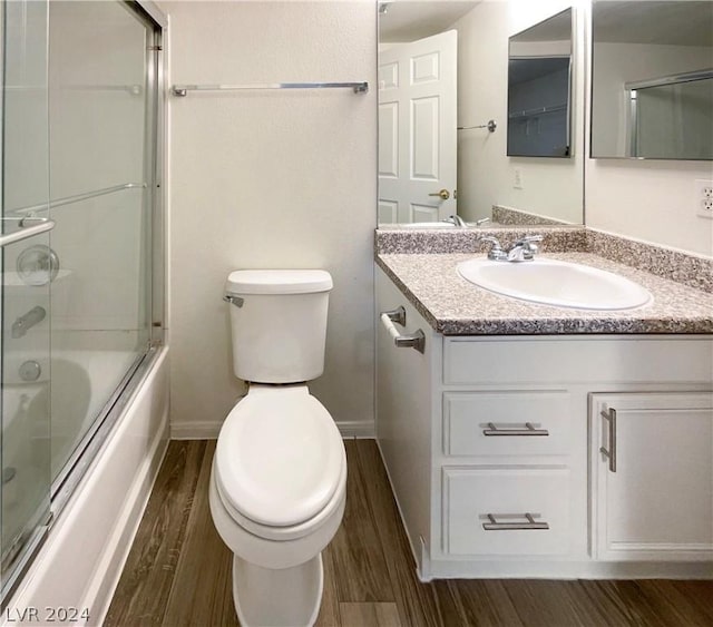 full bathroom with combined bath / shower with glass door, hardwood / wood-style floors, vanity, and toilet