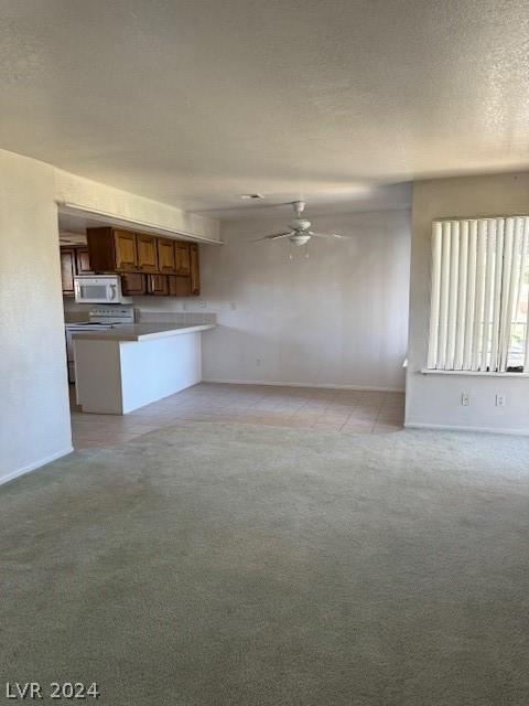 kitchen with ceiling fan, stove, a textured ceiling, light colored carpet, and kitchen peninsula