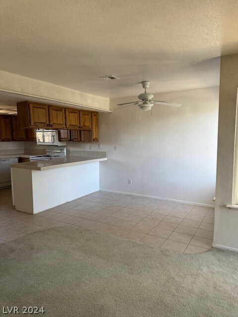 kitchen with a textured ceiling, white appliances, kitchen peninsula, ceiling fan, and light colored carpet